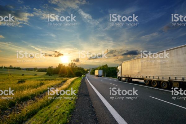 Trucks driving towards the setting sun on a tarmac road in rural countryside